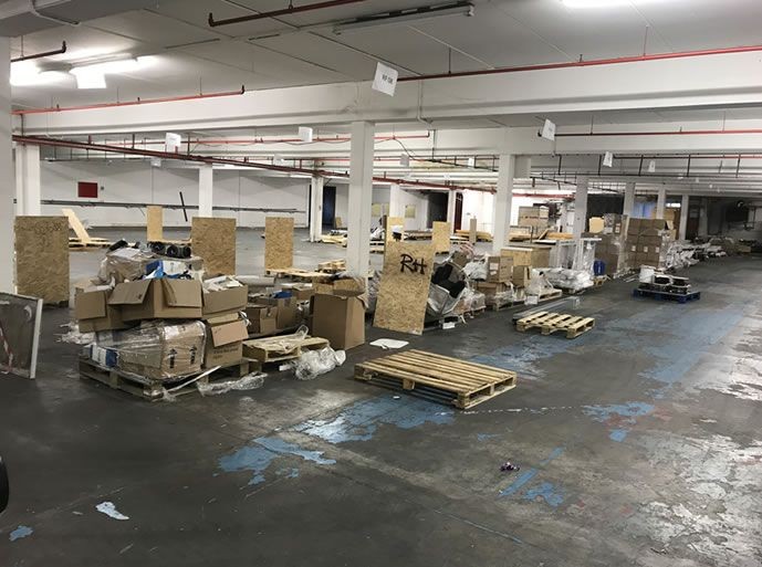 Large warehouse interior with scattered pallets, boxes, and packing materials on the floor.