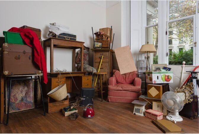 Room filled with various furniture, boxes, and household items stacked in a corner.