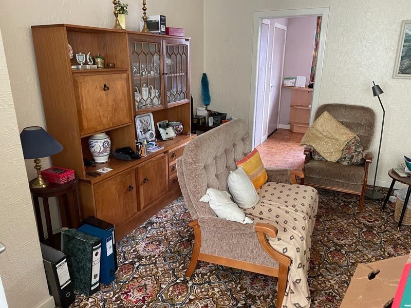 Cozy living room with a vintage sofa, armchair, wooden cabinet, and patterned carpet.